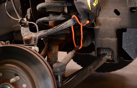 Mechanic wrapping a band around the Chevy Silverado hardware to prop the tie rod end